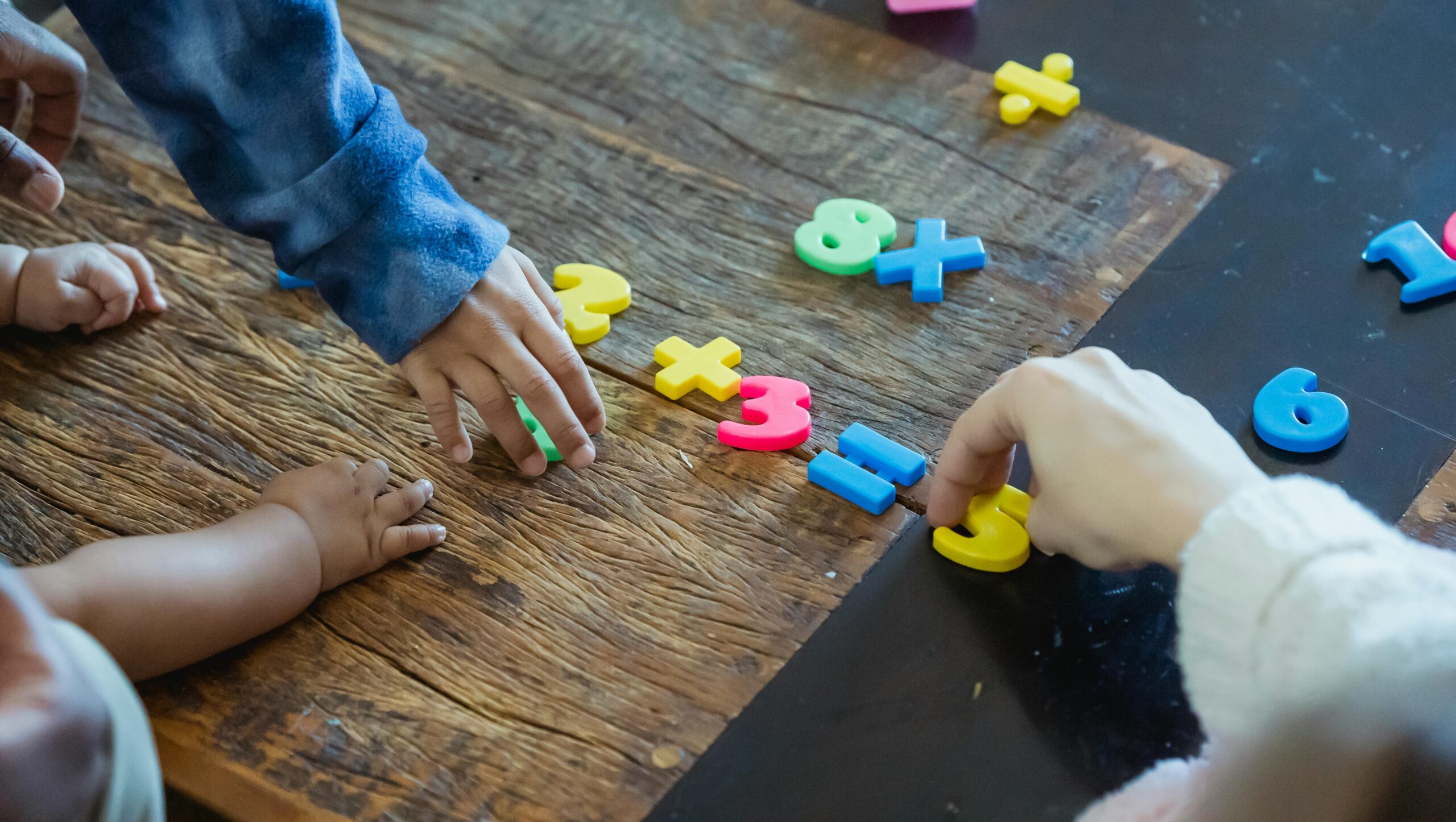 Kids engaging with colorful plastic numbers on a wooden table, fostering early math skills.